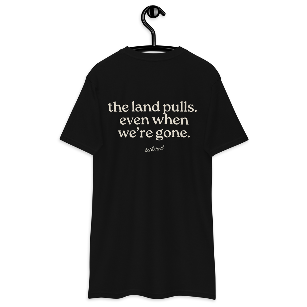 black the land pulls tee hanging on wooden hanger